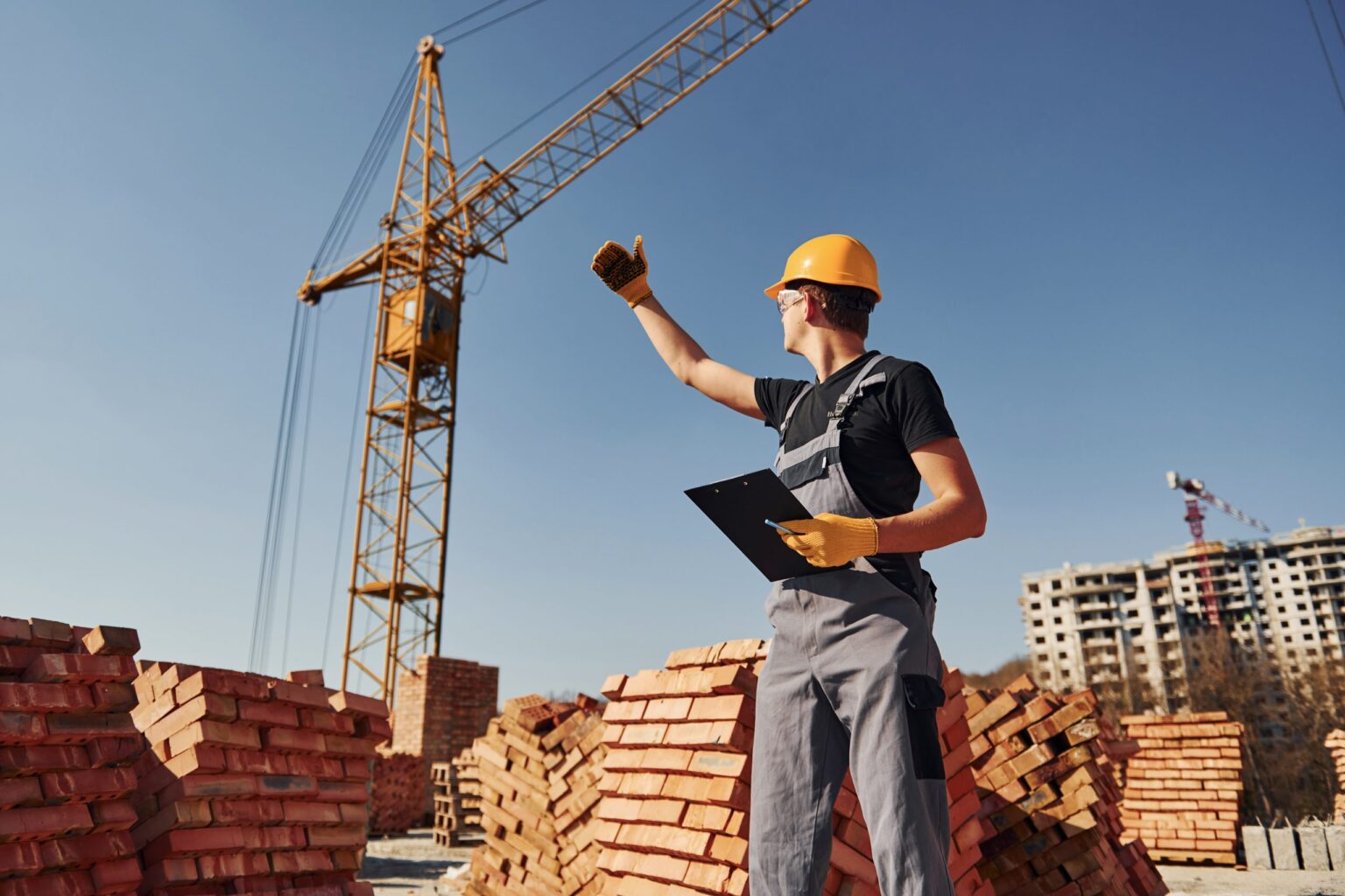 Chef de chantier devant une grue et des palettes de briques, assurance construction avec Roussille Assurances